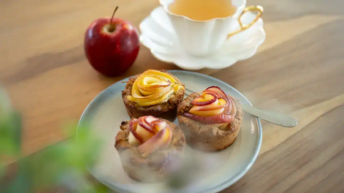 Apfelrosen-Muffins mit Zimt und Äpfeln auf einem Holztisch – herbstliches Gebäck mit Tee, ideal für gemütliche Oktobertage