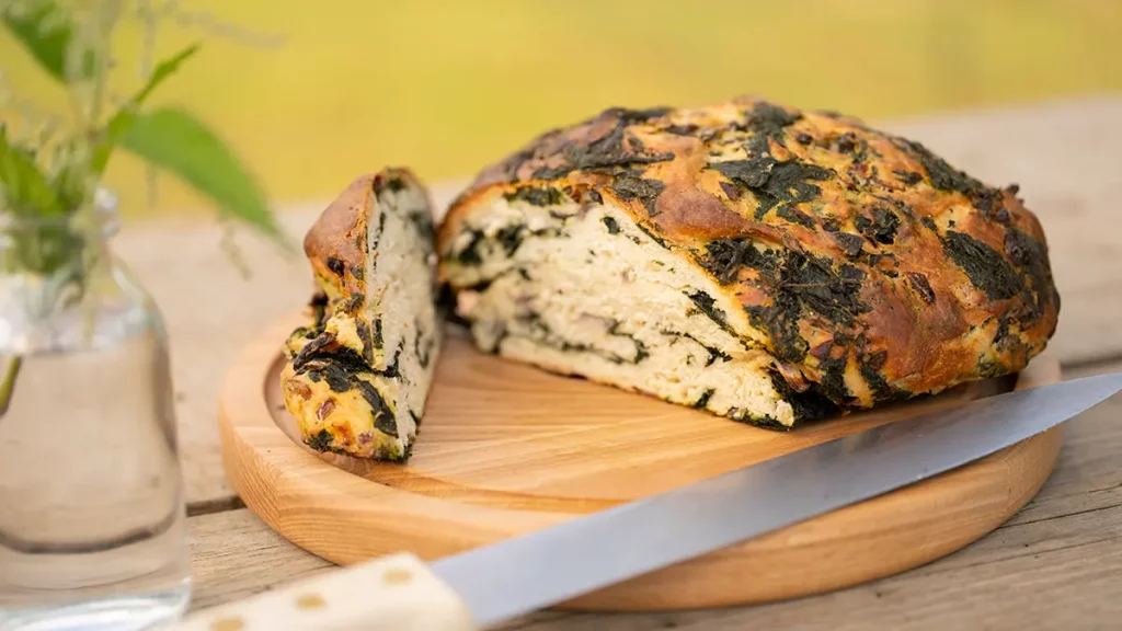 Knuspriges Brennnesselbrot mit frischen Blättern und Samen – frisch gebacken auf Holzbrett