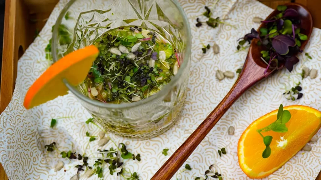 Fruchtig-würziges Orangen-Dressing in einem Glas mit frischen Orangenstücken und Kräutern auf hellem Untergrund