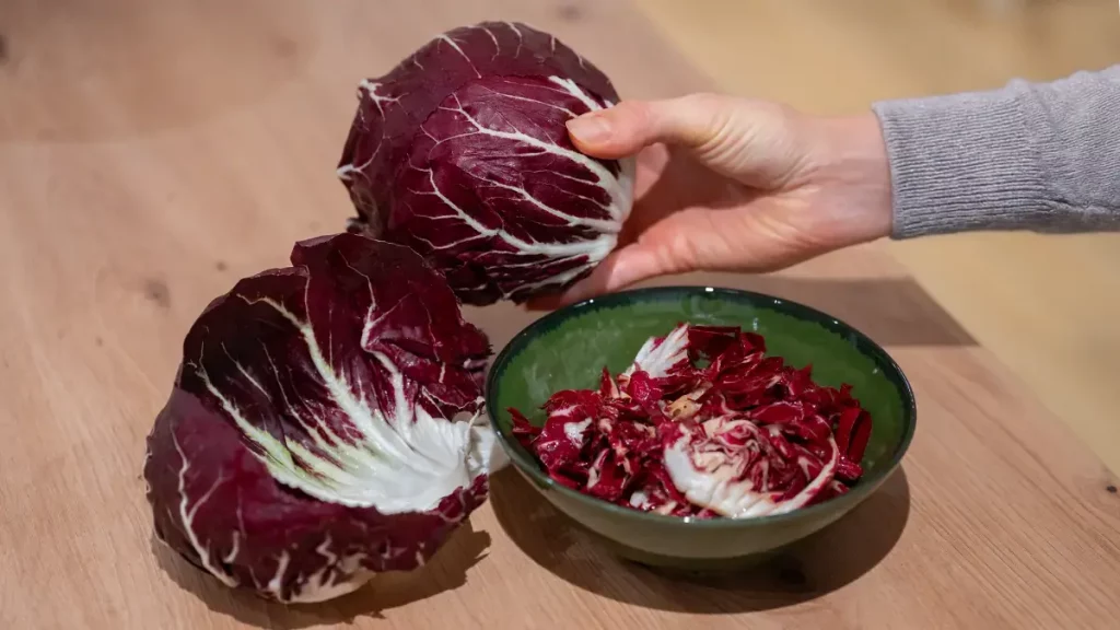 Aufgeschnittener Radicchio und eine Schüssel mit fein geschnittenem Radicchio auf einem Holztisch – typisches Wintergemüse mit intensiver roter Farbe.